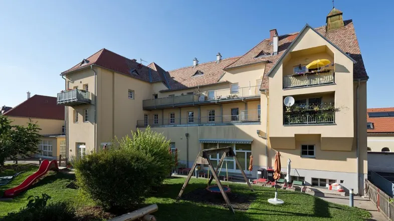 Großzügiger Gartenbereich mit Spielplatz und Balkonen am Mehrfamilienhaus.