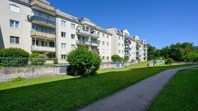 Mehrere Wohngebäude mit Balkonen und einer gepflegten Grünfläche im Vordergrund unter blauem Himmel.