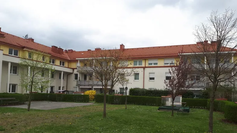 Außenansicht eines Mehrfamilienhauses mit rotem Ziegeldach und gepflegtem Innenhof.