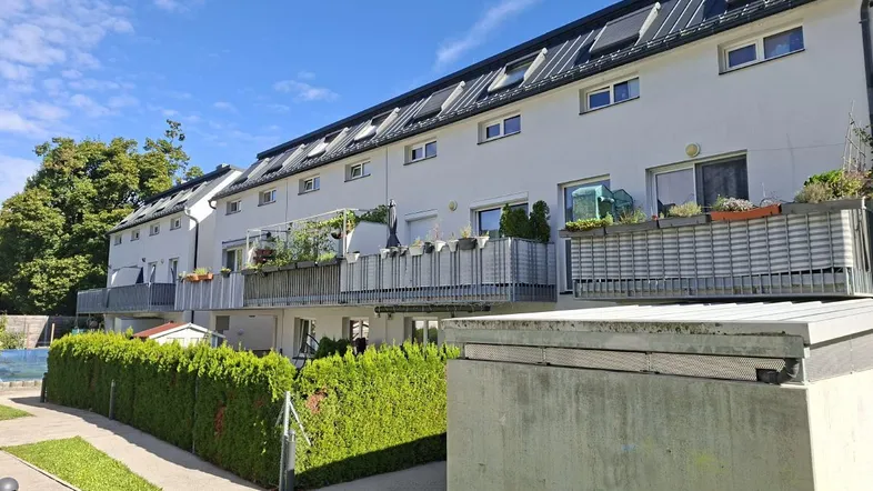 Reihenhäuser mit Balkonen und gepflegter Hecke unter blauem Himmel.