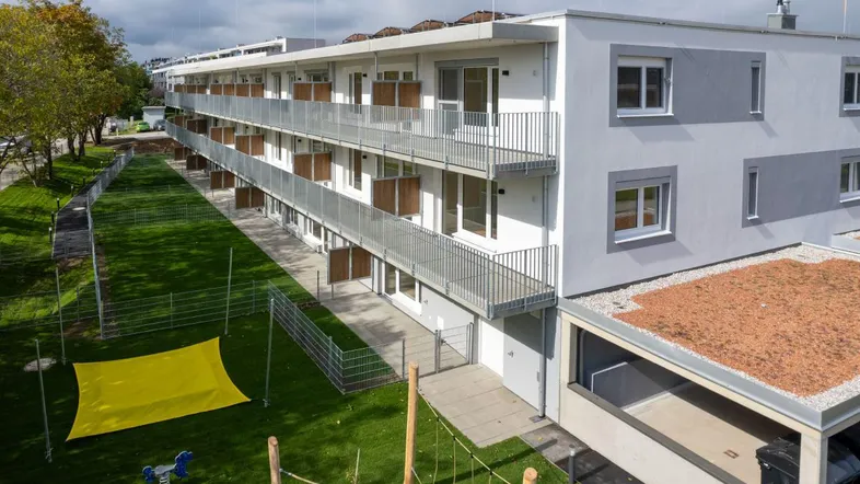 Modernes Mehrfamilienhaus mit Balkonen, Grünflächen und einem kleinen Spielbereich im Freien.