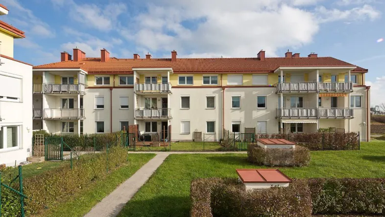 Mehrfamilienhaus mit hellen Fassaden, roten Dächern und gepflegten Grünflächen im Innenhof.