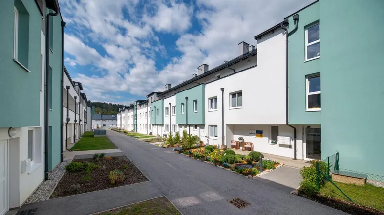 Reihe moderner Reihenhäuser mit hellgrünen und weißen Fassaden unter blauem Himmel und gepflegten Vorgärten.