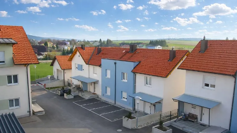 Reihenhäuser mit roten Dächern und blauen Akzenten in einer ländlichen Umgebung unter blauem Himmel.