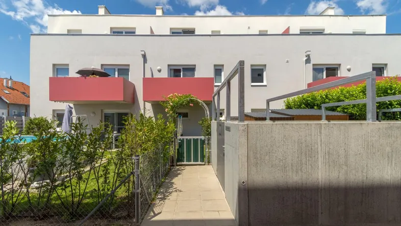 Modernes Mehrfamilienhaus mit roten Balkonen, Grünflächen und Zugangsweg.