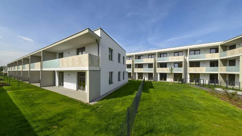 Moderne Wohngebäude mit mehreren Etagen und Balkonen, umgeben von gepflegten Grünflächen unter blauem Himmel.