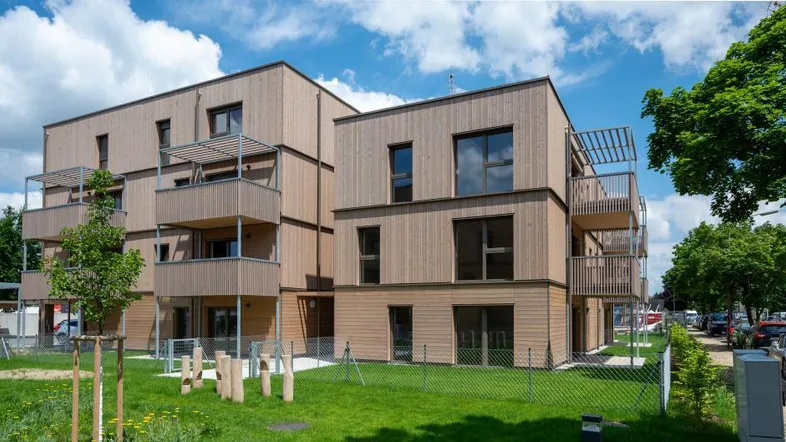 Modernes Mehrfamilienhaus mit Holzfassade, Balkonen und grüner Umgebung unter blauem Himmel.