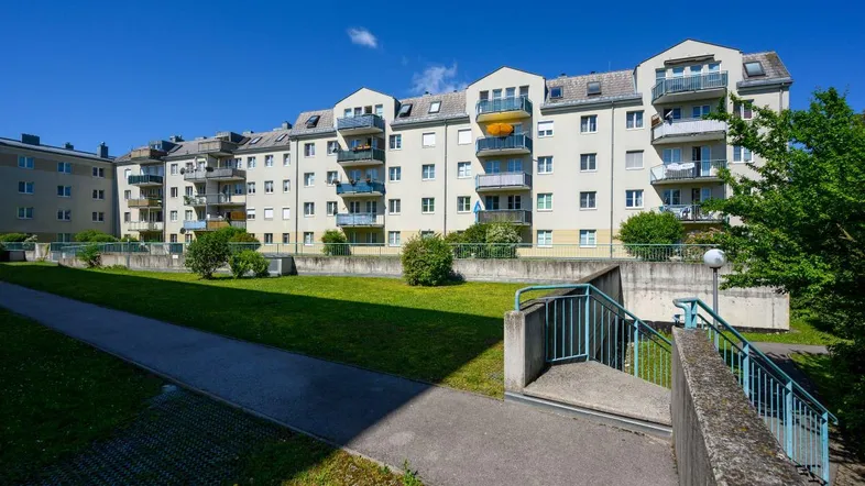 Mehrere Wohngebäude mit Balkonen und einer gepflegten Grünfläche im Vordergrund unter blauem Himmel.