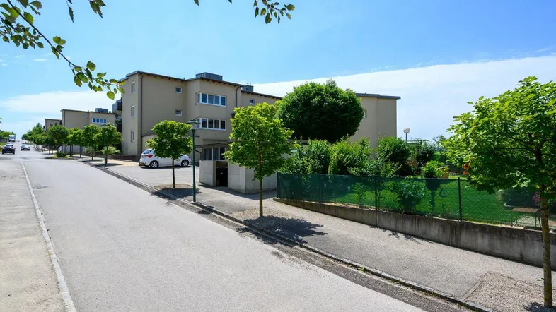 Ansicht eines modernen Wohngebäudes von der Straße mit Bäumen und Parkplätzen.