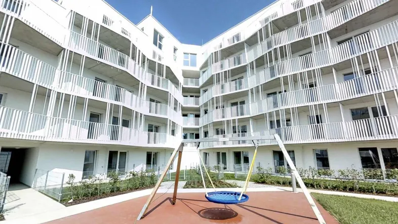 Moderner Wohnkomplex mit weißer Fassade, Balkonen und einem zentralen Spielplatz im begrünten Innenhof.