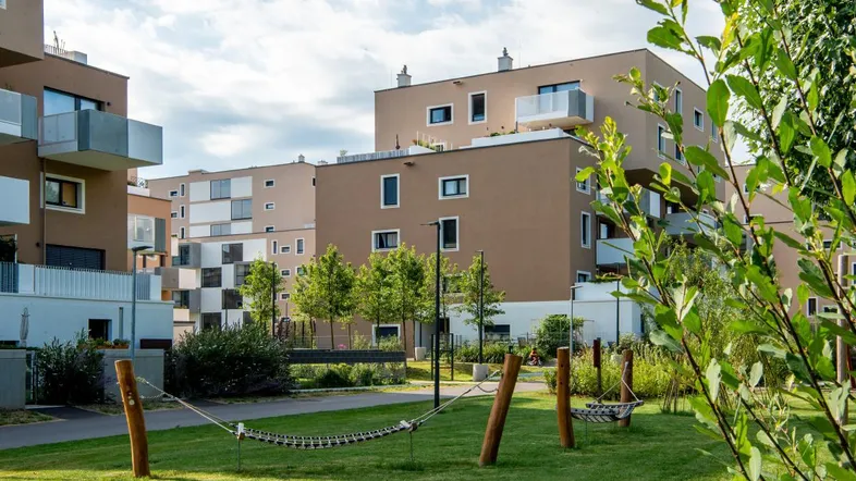 Moderne Wohnanlage mit mehreren Gebäuden, Grünflächen und Hängematten im Freien.