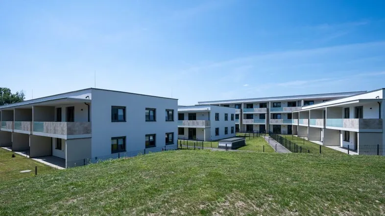 Moderne Mehrfamilienhäuser mit Balkonen und gepflegten Grünflächen unter blauem Himmel.