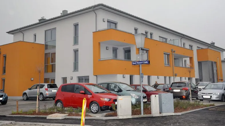 Modernes Mehrfamilienhaus mit orangefarbenen Akzenten und Parkplätzen im Freien.