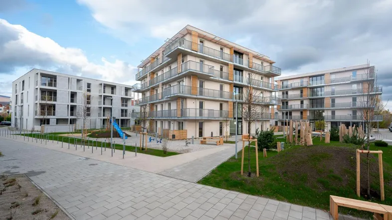 Moderne Wohngebäude mit Balkonen und einem Spielplatz in der Außenanlage unter bewölktem Himmel.