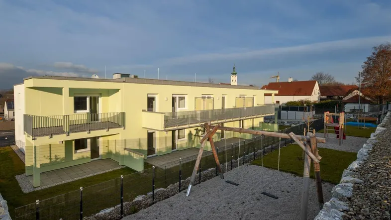 Modernes Mehrfamilienhaus mit Balkonen, Terrassen und einem Spielplatz für Kinder.
