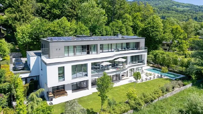 Moderne Villa mit Flachdach, Solaranlage, großem Garten und Außenpool in grüner Umgebung.