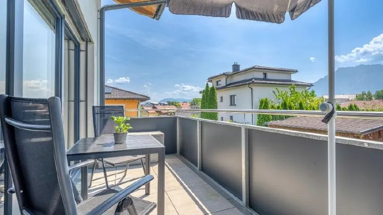 Heller Balkon mit Sitzgelegenheiten, Sonnenschirm und weitem Blick auf die Berge und Umgebung.