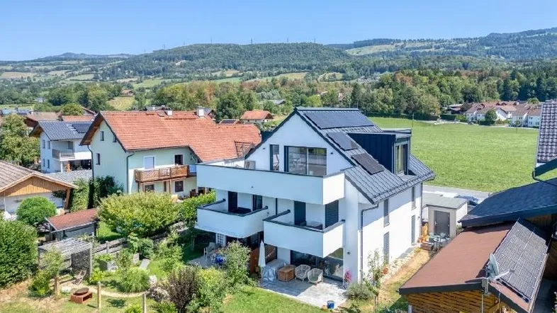 Modernes Wohnhaus mit Balkonen, Solaranlage und Garten in ländlicher Umgebung mit Bergblick.