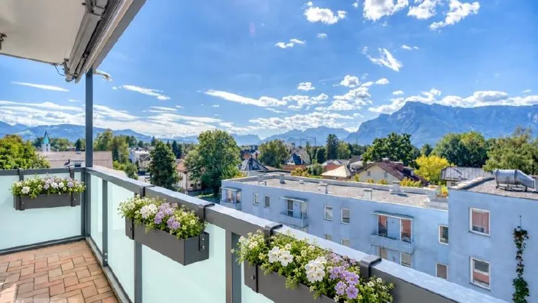 Heller Balkon mit Ziegelboden, Blumenkästen und weitem Blick auf die Berge und die grüne Umgebung.