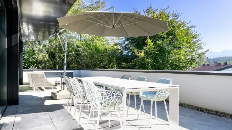 Große, sonnige Terrasse mit Esstisch, Sonnenschirm und Blick ins Grüne.