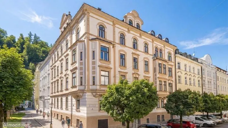 Historisches Gebäude mit reich verzierter Fassade an einer belebten Straße mit Bäumen und parkenden Autos.