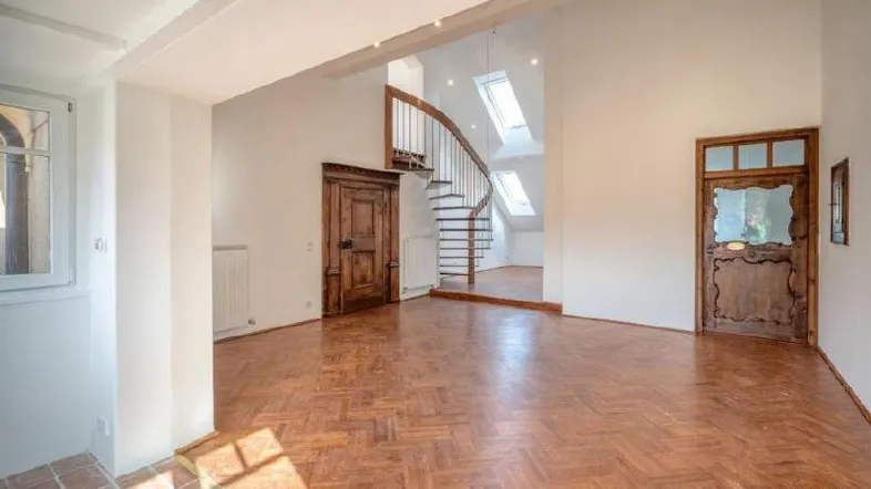 Heller Wohnbereich mit Holzparkett, Wendeltreppe und historischen Holztüren, beleuchtet durch Dachfenster.