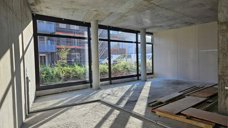 Unfertiger Innenraum eines Neubaus mit großen Fenstern und Betonwänden, bereit für den Ausbau.