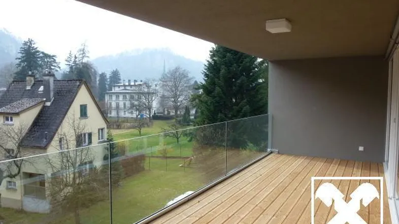 Geräumiger Balkon mit Holzboden, Glasbrüstung und weitem Blick ins Grüne.
