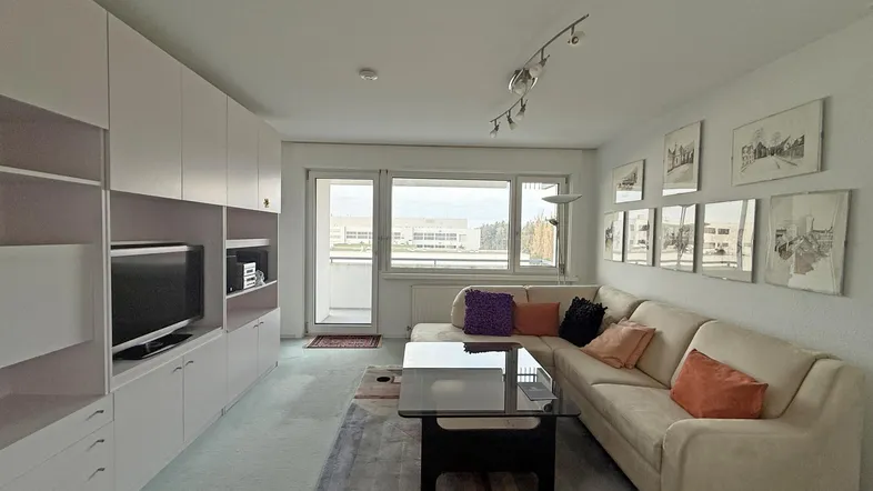 Helles Wohnzimmer mit beiger Couch, weißen Einbauschränken und Zugang zum Balkon.