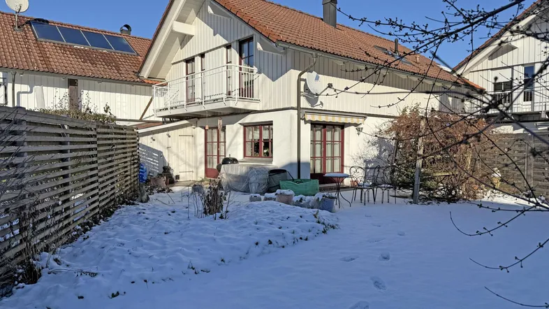 Weißes Einfamilienhaus mit rotem Ziegeldach, Balkon und verschneitem Garten im Winter.