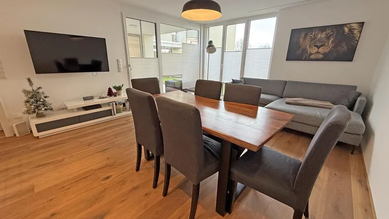 Heller Wohn- und Essbereich mit Holztisch, bequemer Couch und großen Fenstern für viel Tageslicht.