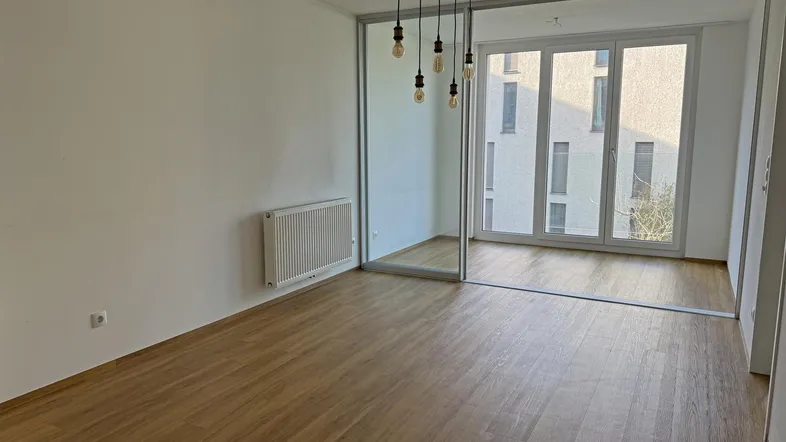 Helles Zimmer mit Laminatboden, großen Fenstern und einem modernen Deckenlicht.