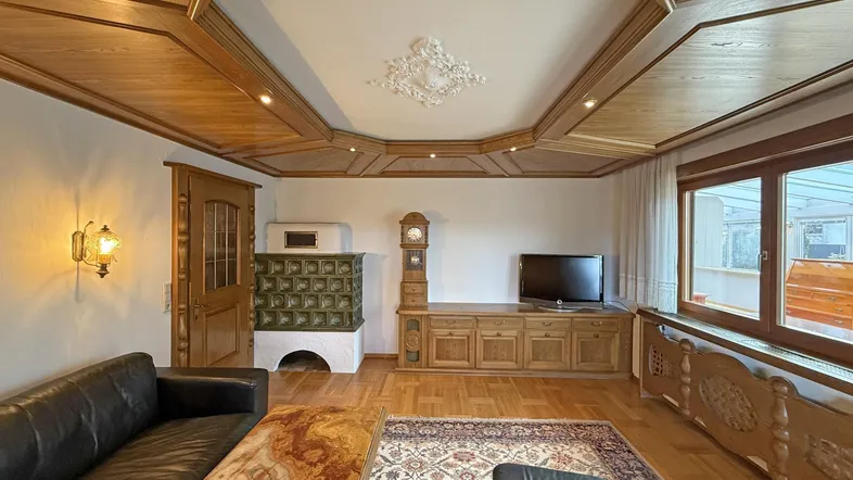 Helles Wohnzimmer mit Holzkassettendecke, Parkettboden und Kachelofen.