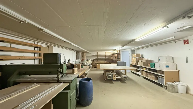 Geräumiger Werkstattbereich mit Holzbearbeitungsmaschinen und Lagerregalen, gut beleuchtet und funktional.