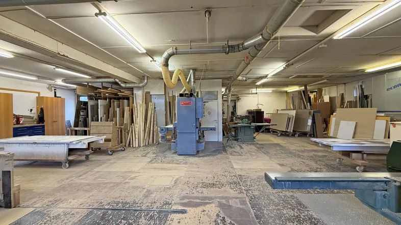 Weitläufiger Werkstattbereich mit Holzmaterialien und Maschinen, gut organisiert und für Arbeiten bereit.