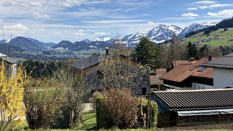 Panoramablick auf die umliegende Berglandschaft und das Dorf mit grünen Hügeln und schneebedeckten Gipfeln.