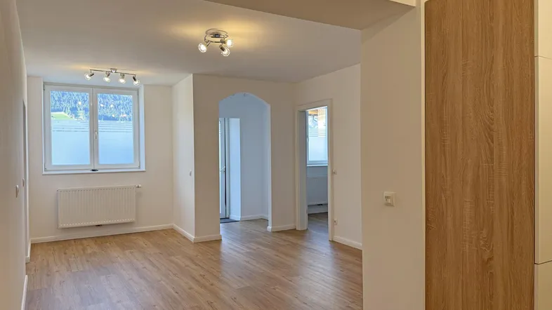 Heller Wohnbereich mit modernem Laminatboden und Blick auf die grüne Umgebung durch die Fenster.