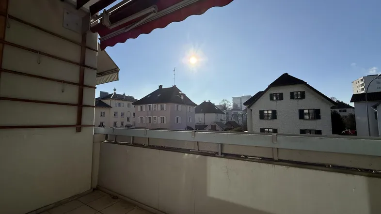 Helles Balkon mit Fliesenboden und Blick auf umliegende Gebäude unter blauem Himmel.
