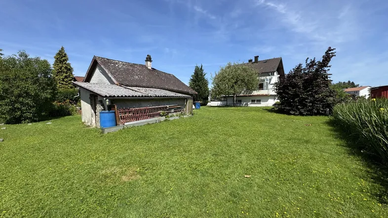 Großer Gartenbereich mit Rasenfläche und einem Nebengebäude unter blauem Himmel.