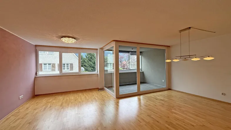 Geräumiges Wohnzimmer mit hellem Parkettboden und einem verglasten Bereich, der als Loggia dient.