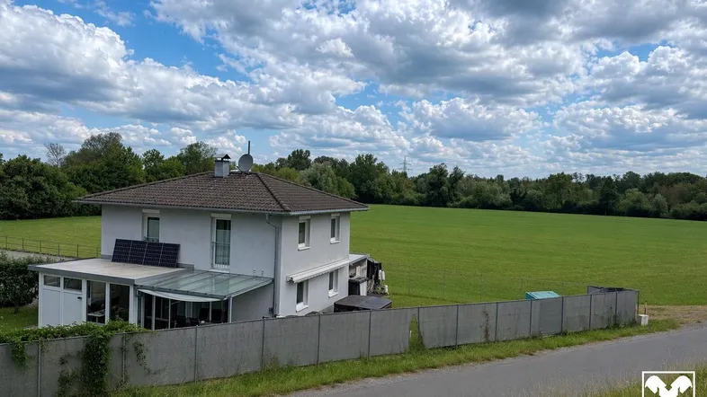 Einfamilienhaus mit Photovoltaikanlage und weitem Blick auf grüne Felder unter blauem Himmel.