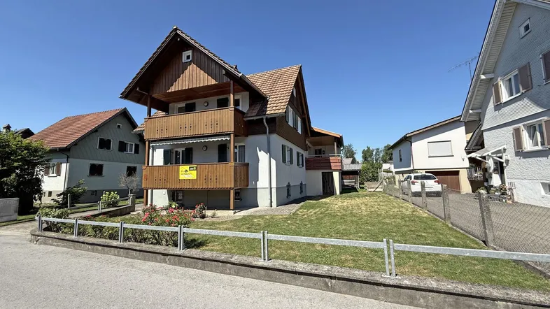Außenansicht eines gepflegten Hauses mit Holzbalkon und Satteldach in sonniger Wohngegend.
