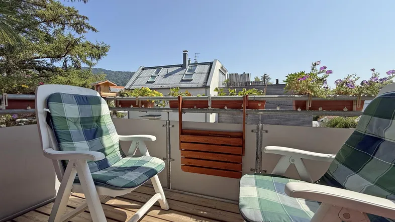 Heller Balkon mit Holzfußboden und Gartenmöbeln, ideal zum Entspannen im Freien mit Blick auf die Umgebung.