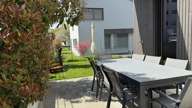 Moderne Terrasse mit Esstisch und Stühlen, umgeben von einem gepflegten Garten und Hecken.