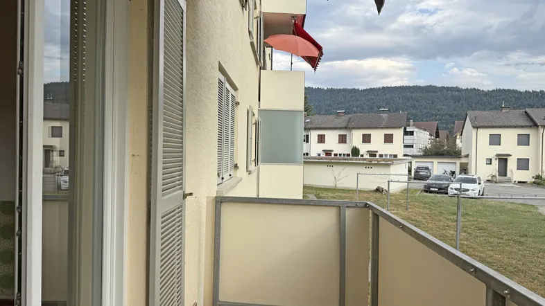Balkon mit Fliesenboden und Blick auf die umliegenden Wohnhäuser und grüne Hügel.