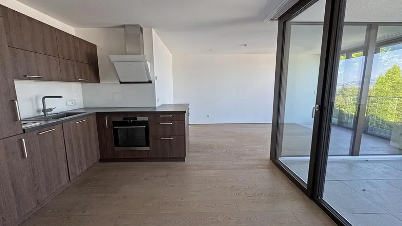 Moderne Einbauküche mit dunklen Holzfronten und offenem Übergang zum Wohnbereich mit Balkonzugang.