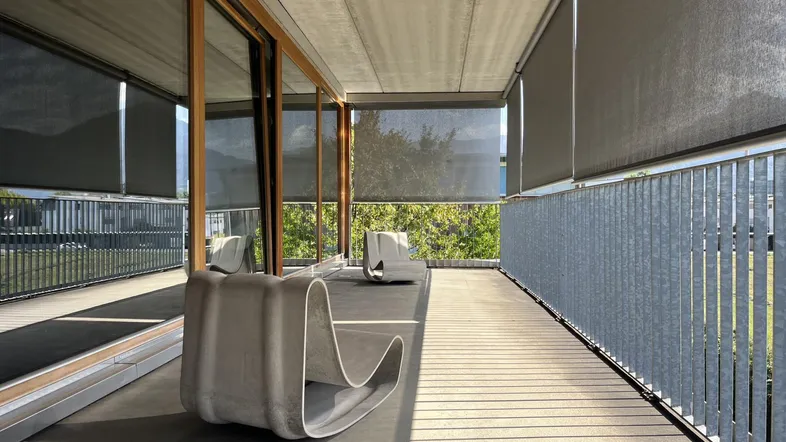 Langer, überdachter Balkon mit modernen Liegen und Blick ins Grüne, ausgestattet mit Sonnenschutzrollos.