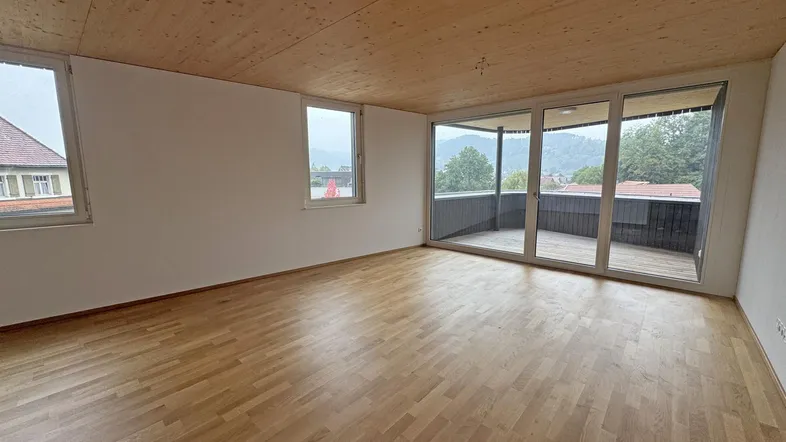 Helles Zimmer mit Holzboden und Zugang zu einem großen Balkon mit Bergblick.