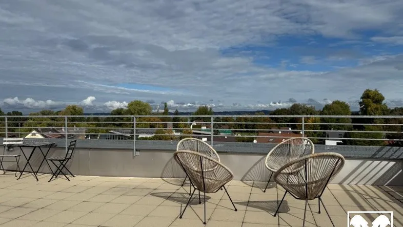 Geräumige Dachterrasse mit Fliesenboden, modernen Sitzgelegenheiten und weitem Blick über die Landschaft und einen See.