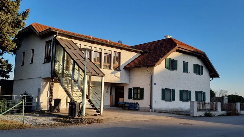 Außenansicht des Hauses mit weißer Fassade, grünen Fensterläden und Außentreppe.